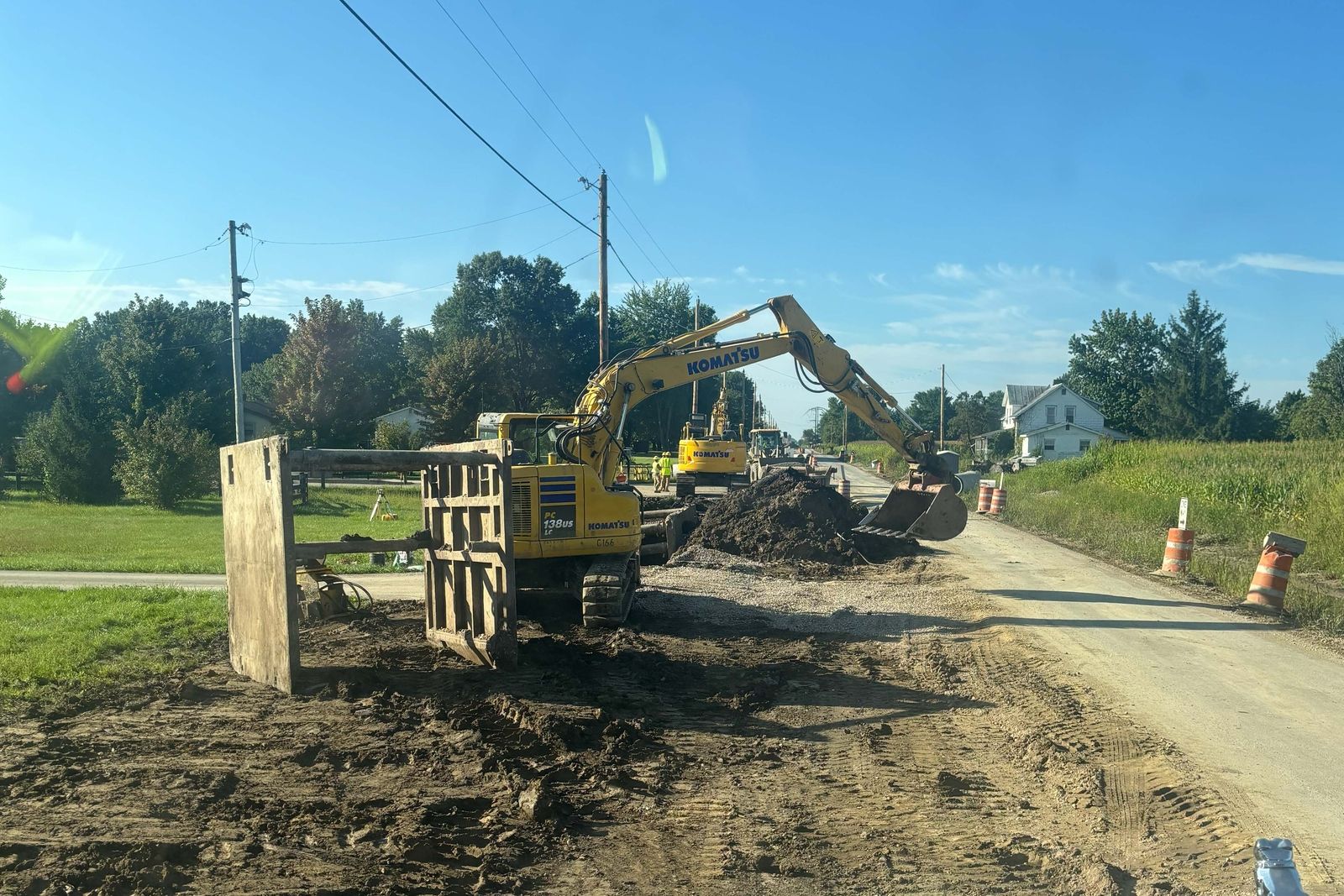 Trench box being set beside a torn up road shoulder