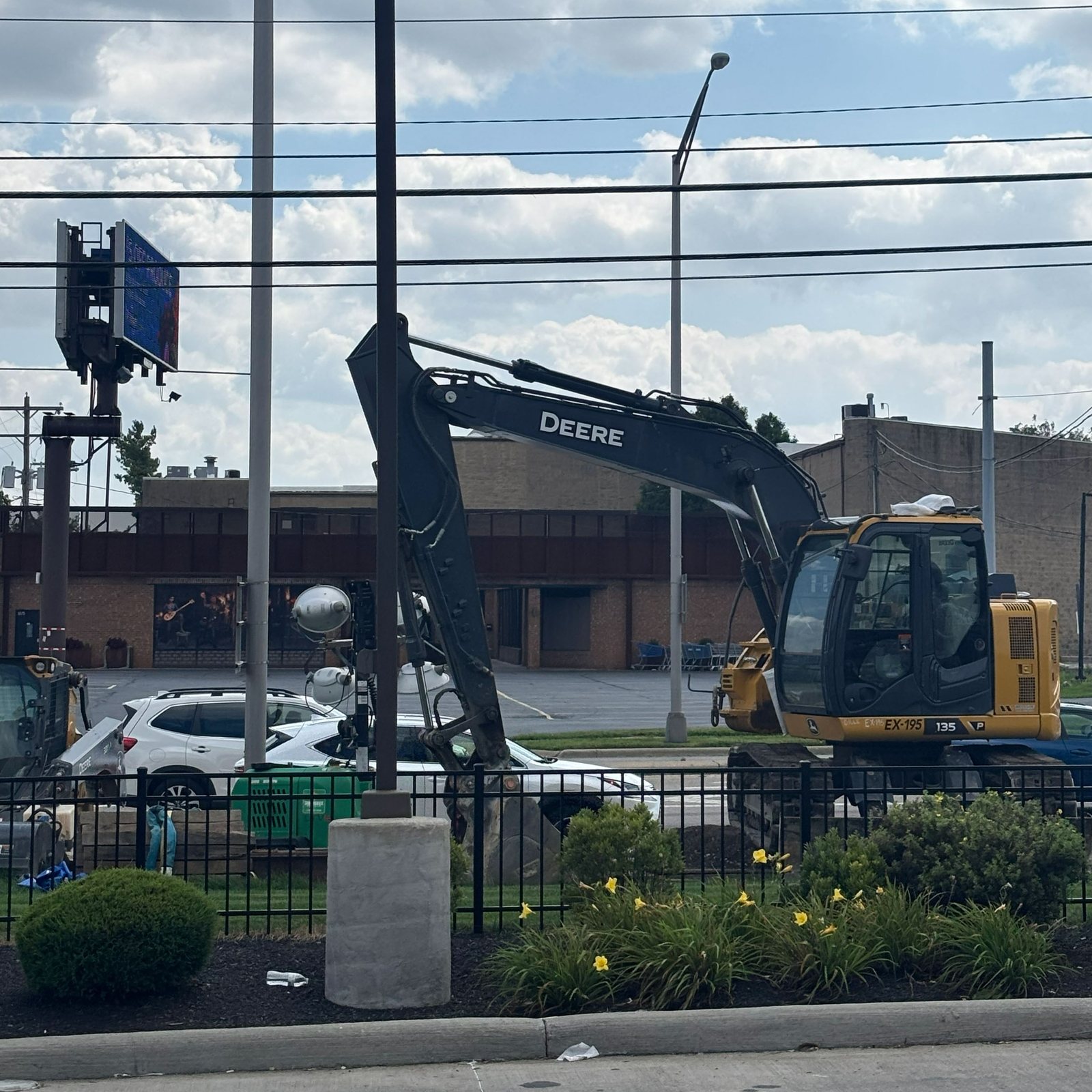 Deere excavator working a fenced storefront corner
