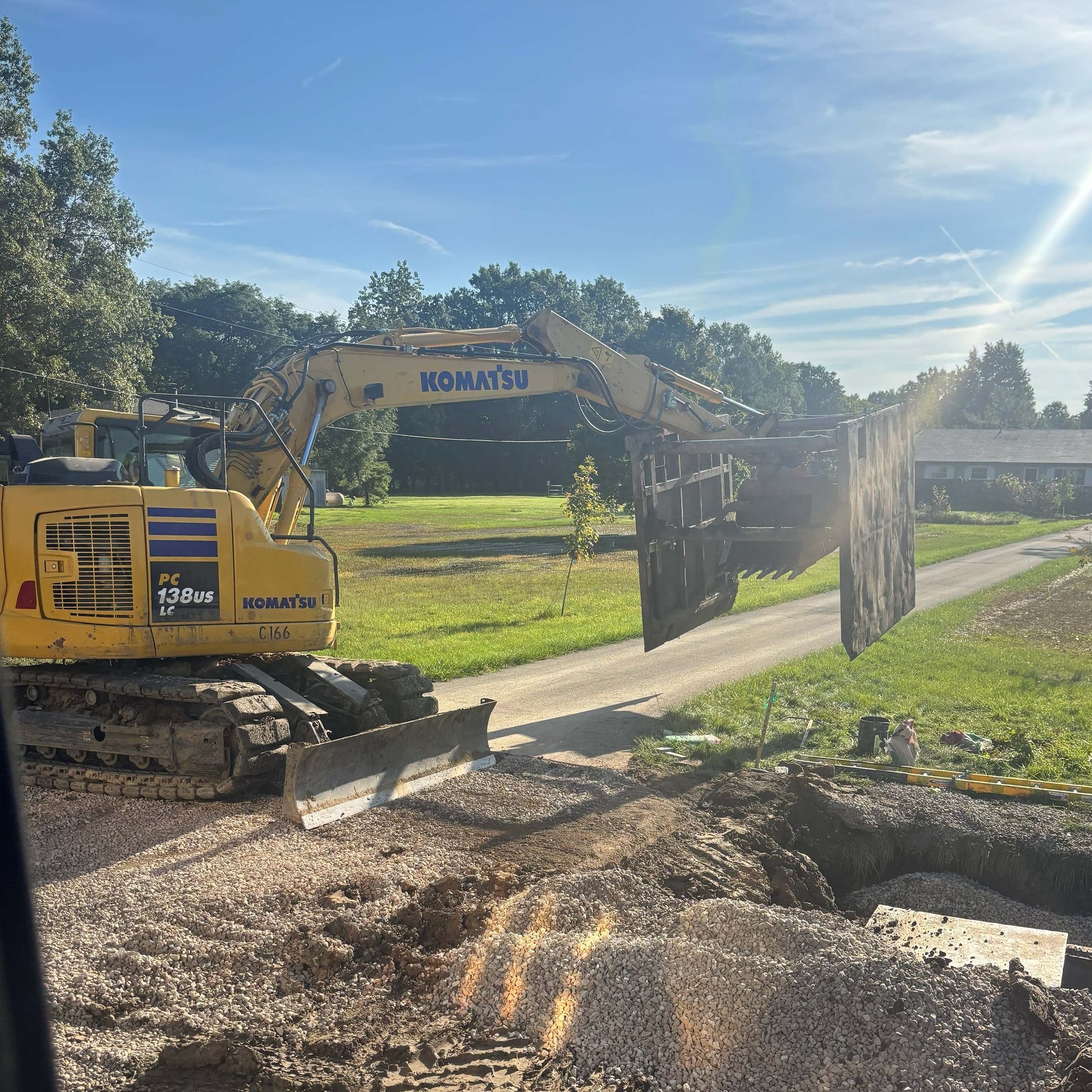 An excavator setting a trench shield beside a gravel drive