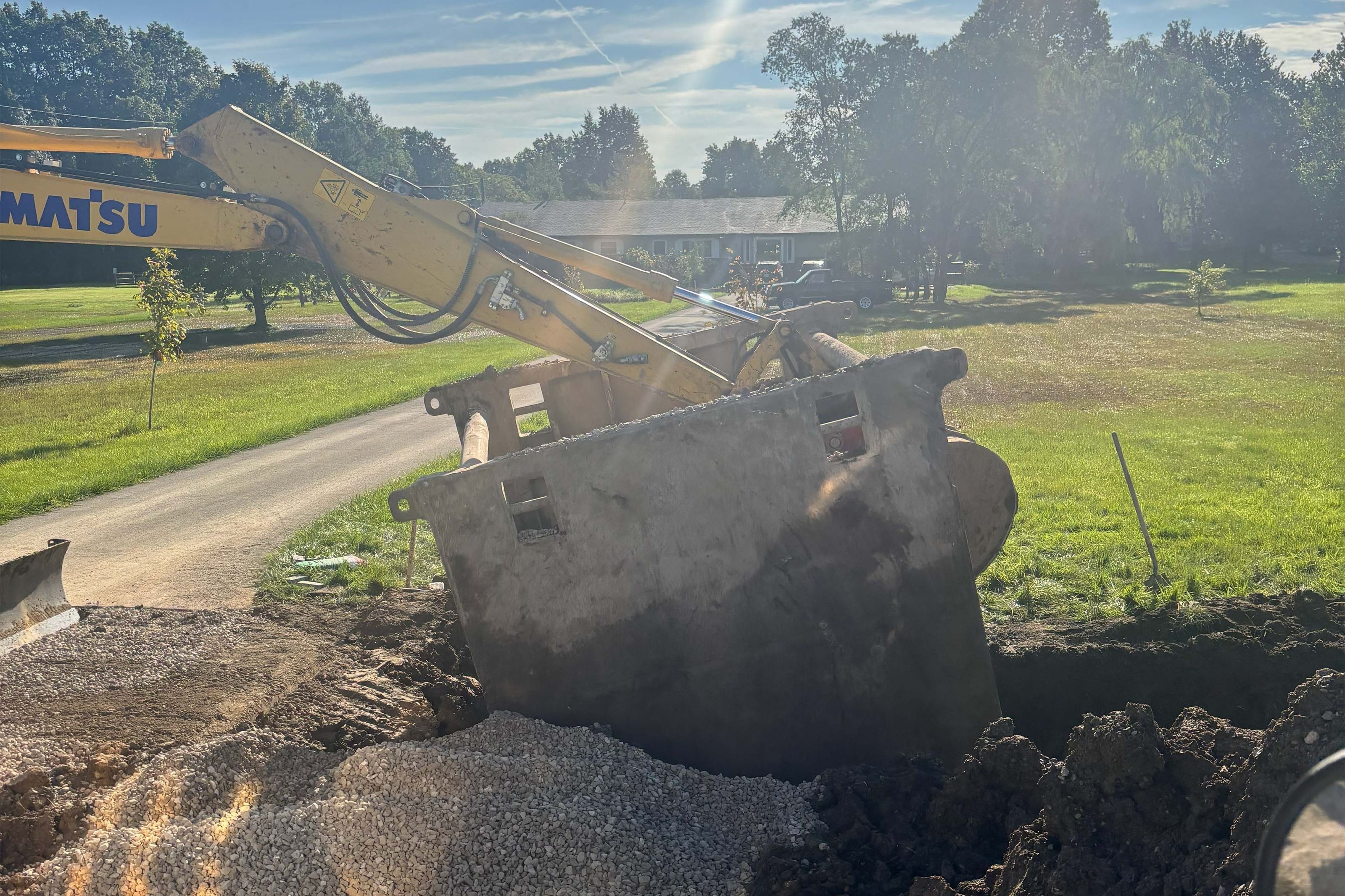 Excavator setting a vault over fresh gravel at a residential job